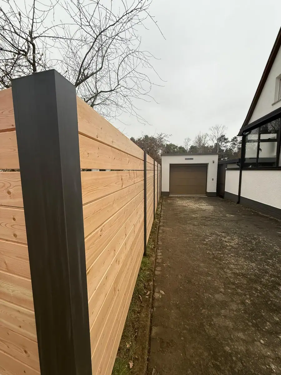 Neu errichteter Holzzaun mit Aluminiumpfosten an einer Einfahrt